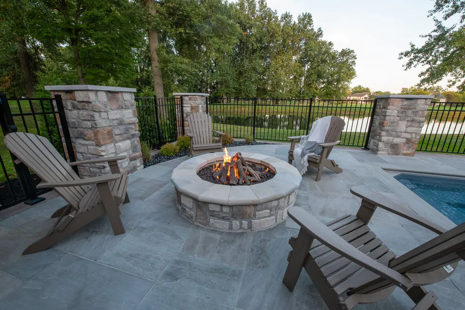 Round fire feature with Adirondack chairs on a poolside paver terrace in Blacklick